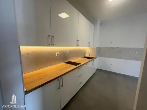 Moderna kuhinja sa belim elementima i drvenom radnom površinom. - image 7