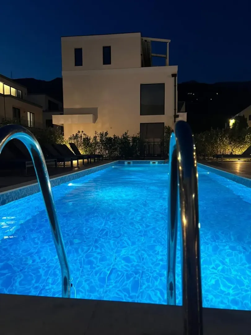 Noćni pogled na osvijetljeni bazen ispred moderne kuće.