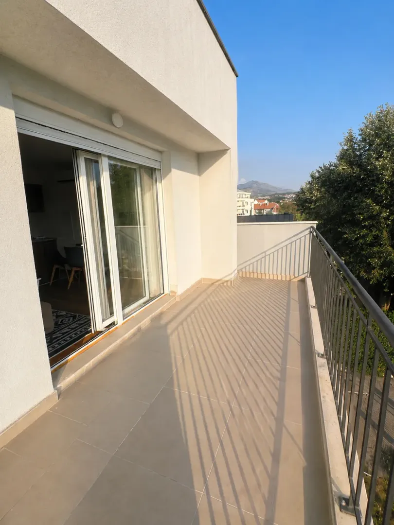 Prostrana terasa sa pločicama i metalnom ogradom.