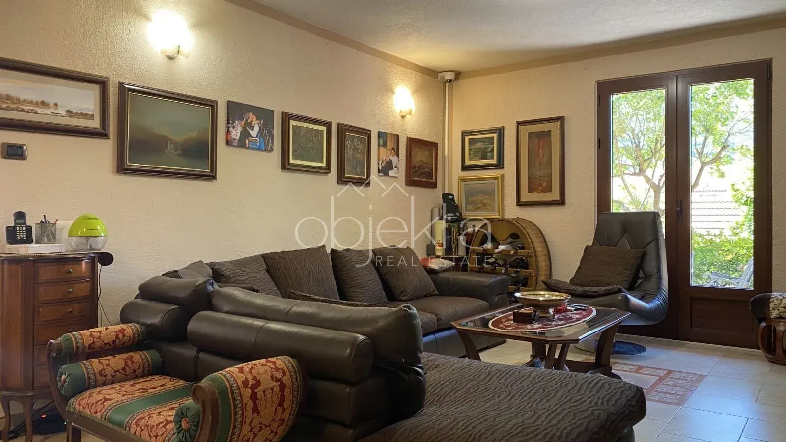 Living room with a sofa set, armchair, and walls decorated with paintings.