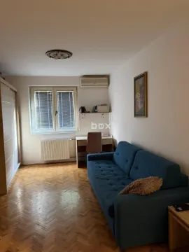 Dnevna soba sa plavim kaučem, radnim stolom i prozorom. - image 2