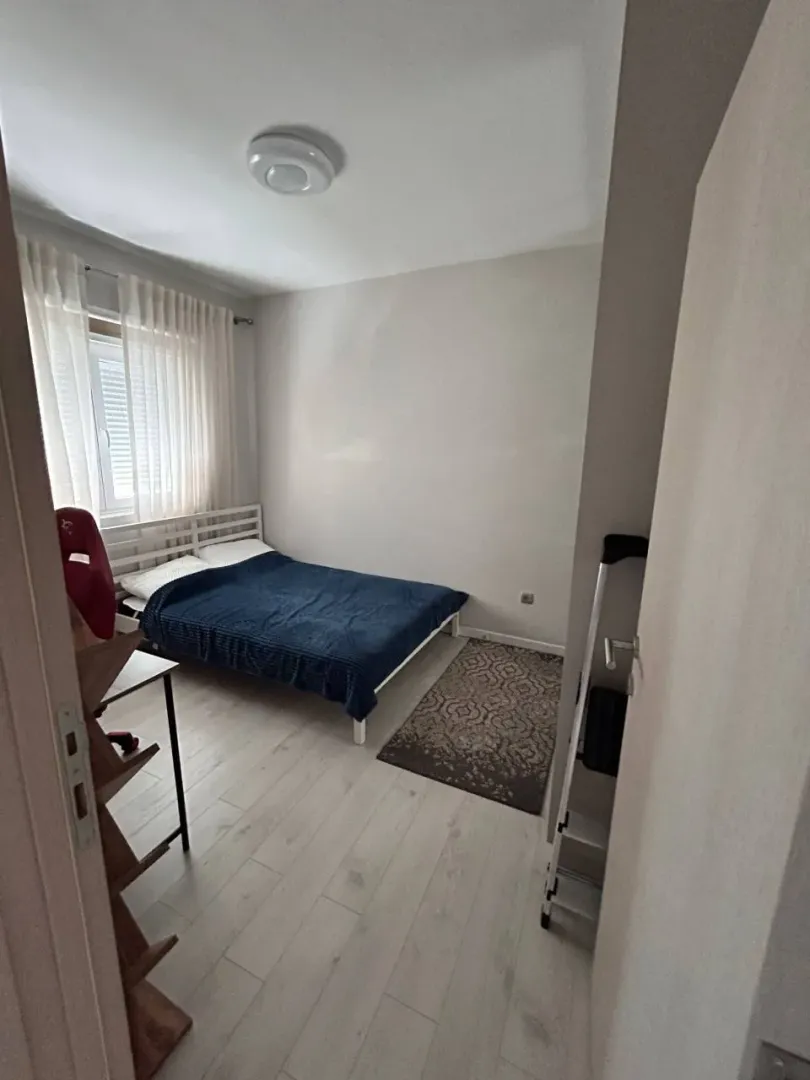 Manja spavaća soba sa krevetom, bijelim podom i prozorom sa zavjesama.