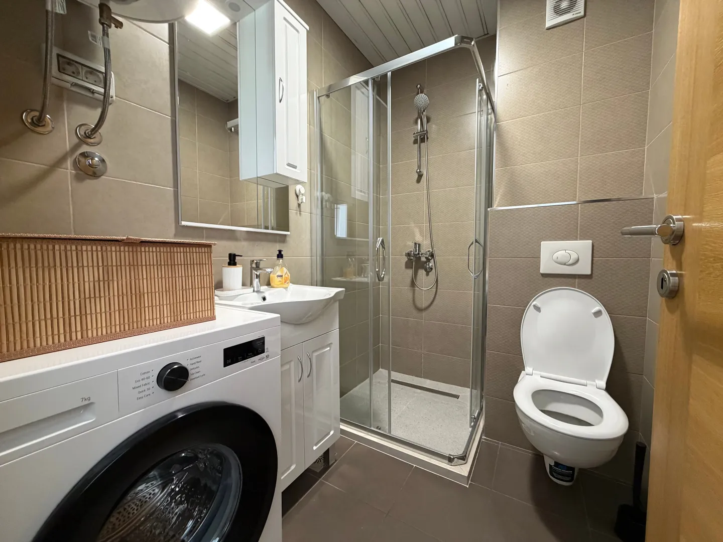 Smaller bathroom with a shower cabin, sink, and washing machine.