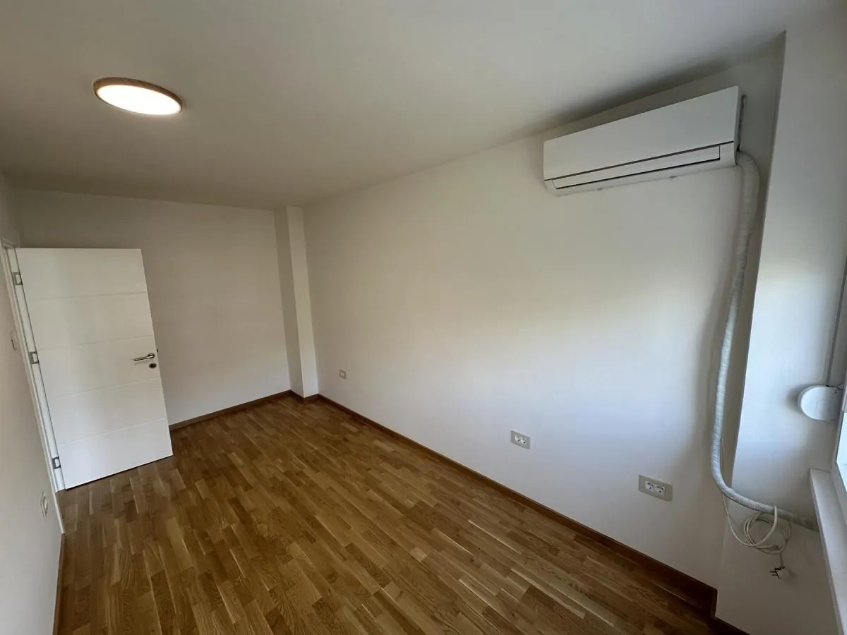 Prazna soba sa parketom i klima uređajem na zidu.