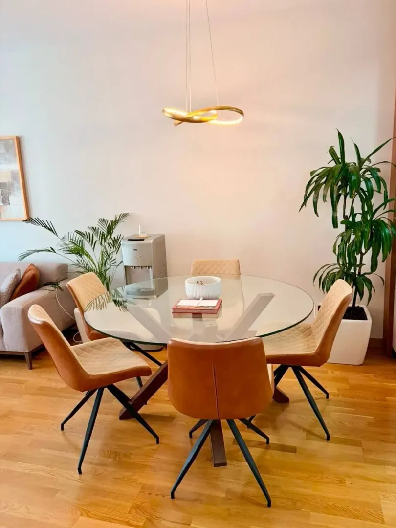 Trpezarija sa okruglim staklenim stolom i modernim stolicama.