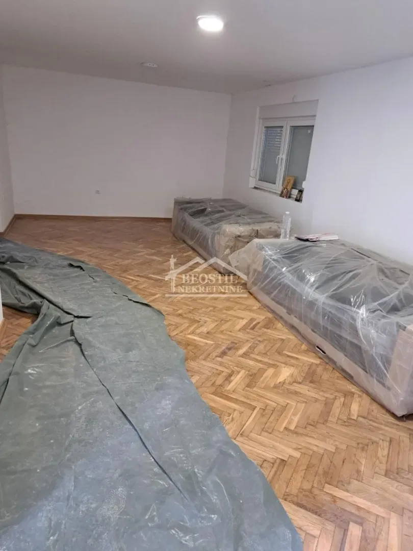 Prazna soba sa parketom i nameštajem prekrivenim zaštitnom folijom.