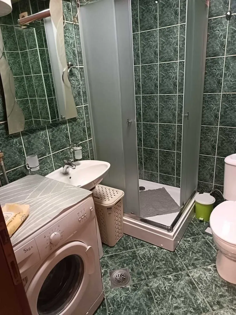 Small bathroom with a shower cabin, washbasin, washing machine, and toilet.