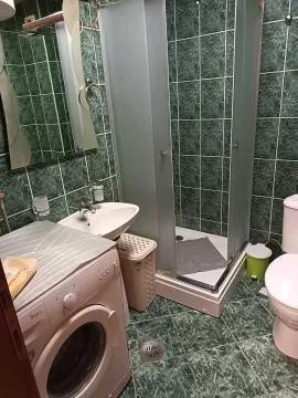 Small bathroom with a shower cabin, washbasin, washing machine, and toilet. - image 9