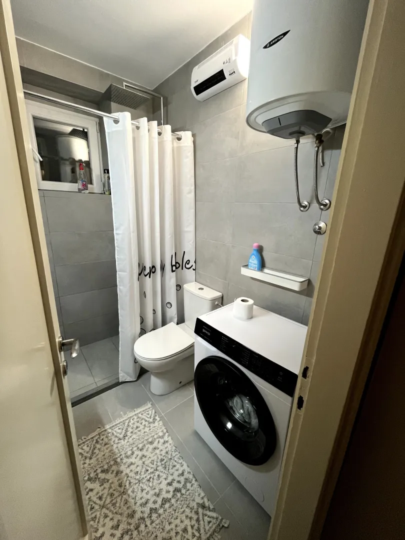 Manje kupatilo sa tuš kabinom, veš mašinom i sanitarijama.