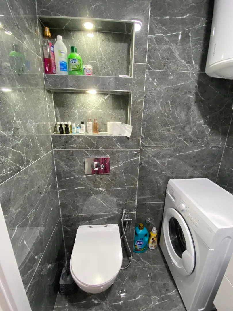 Moderne kupatilo obloženo sivim pločicama sa ugradnom šoljom i veš mašinom.
