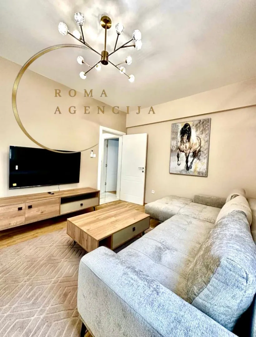 Dnevna soba sa garniturom, TV komodom i modernim lusterom.