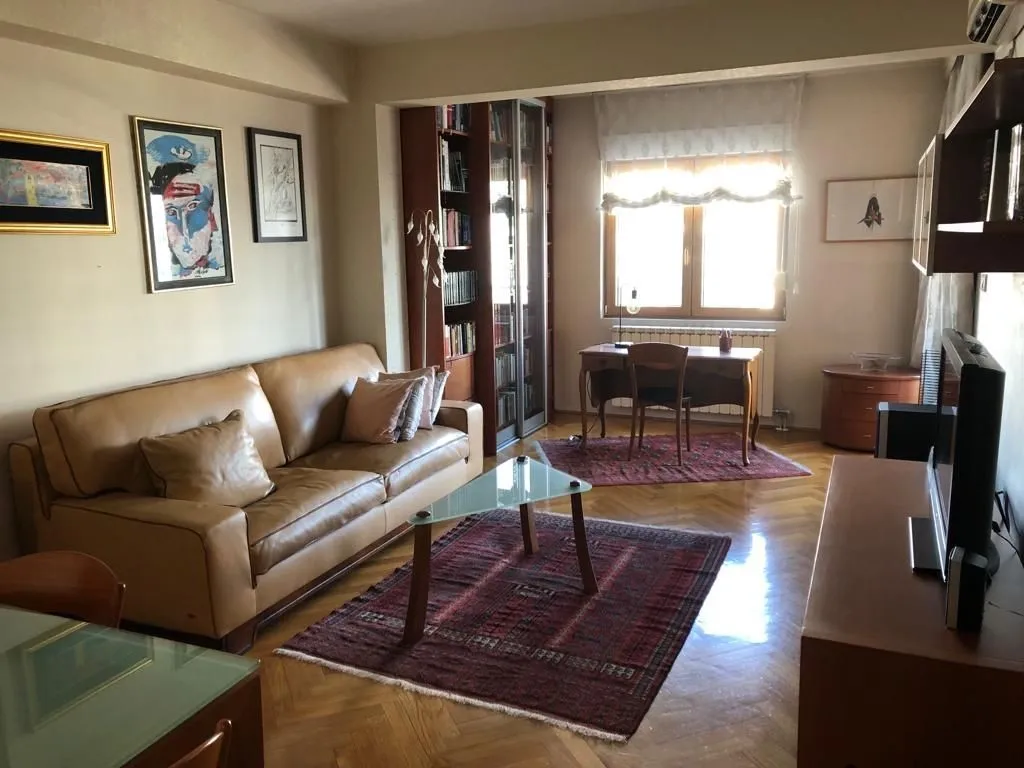 Bright living room featuring a leather sofa, a study desk by the window, and a bookshelf.