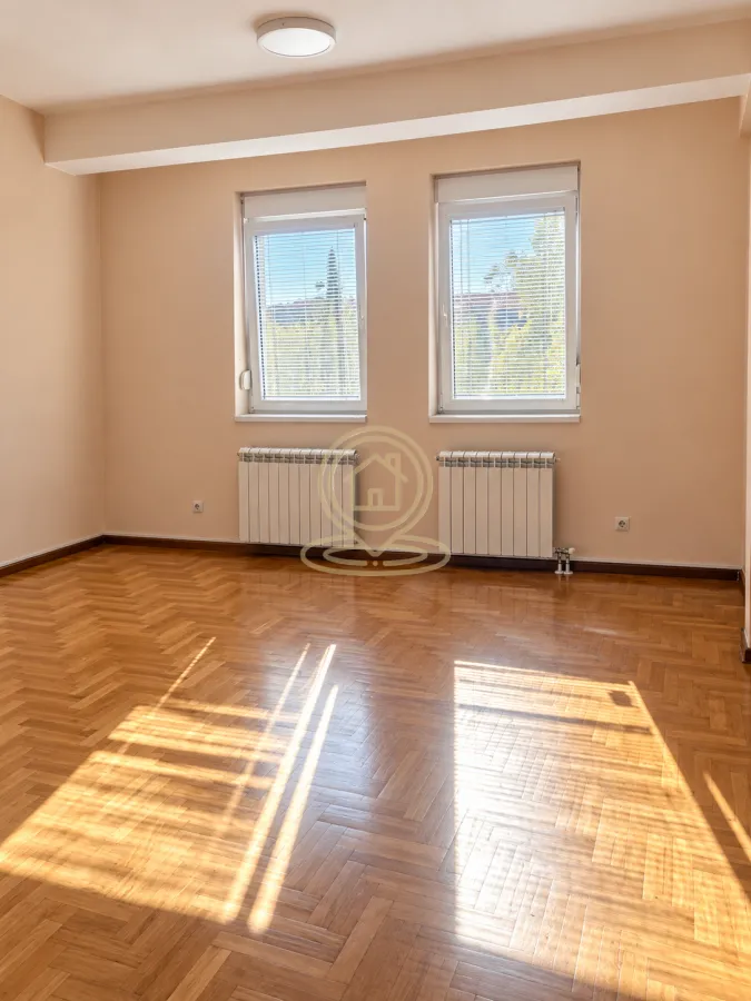 Empty room with wooden parquet flooring, two windows, and radiators.