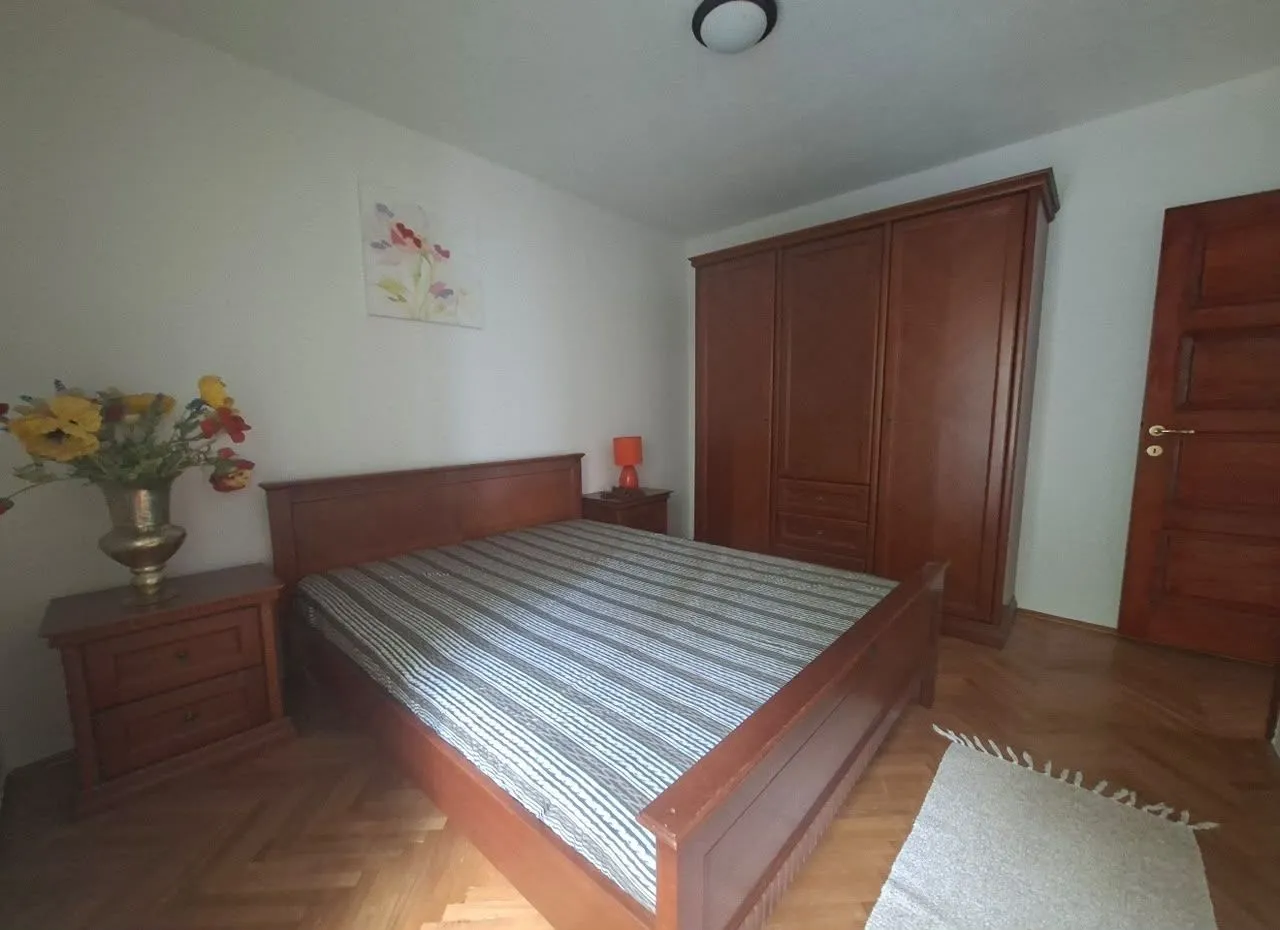 Namještena spavaća soba sa bračnim krevetom, drvenim ormarom i parketom.