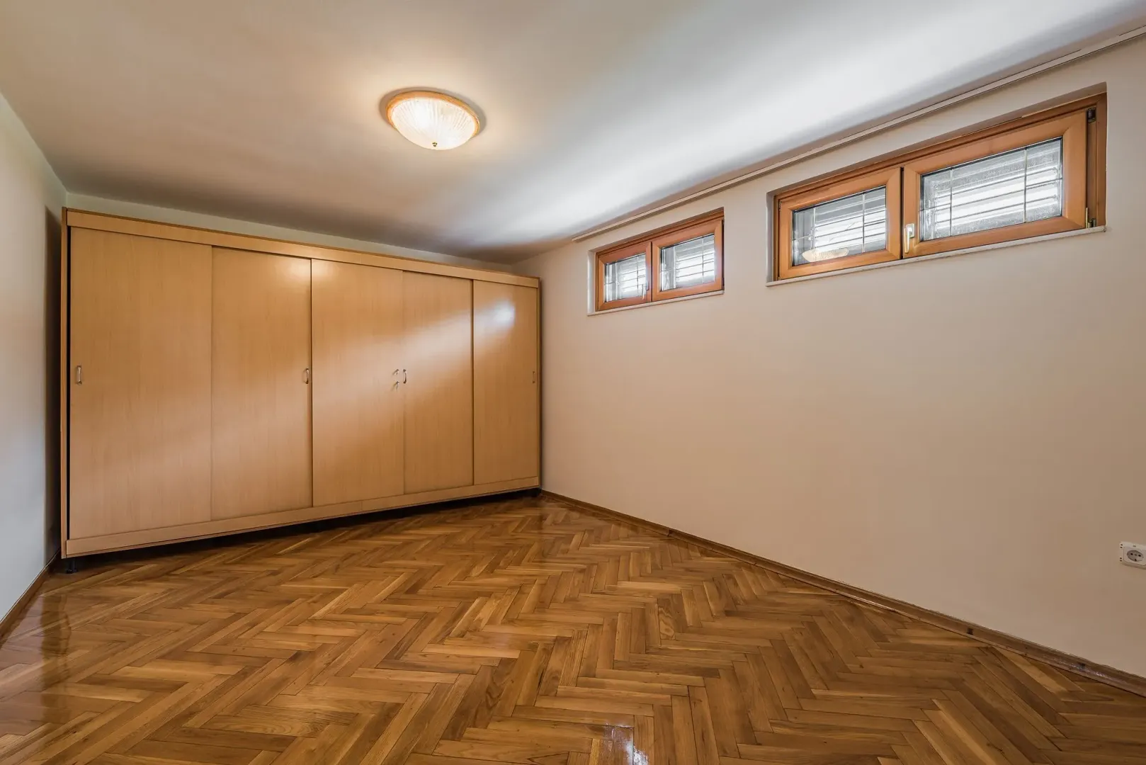 An empty room with a large wooden wardrobe and well-maintained parquet flooring.