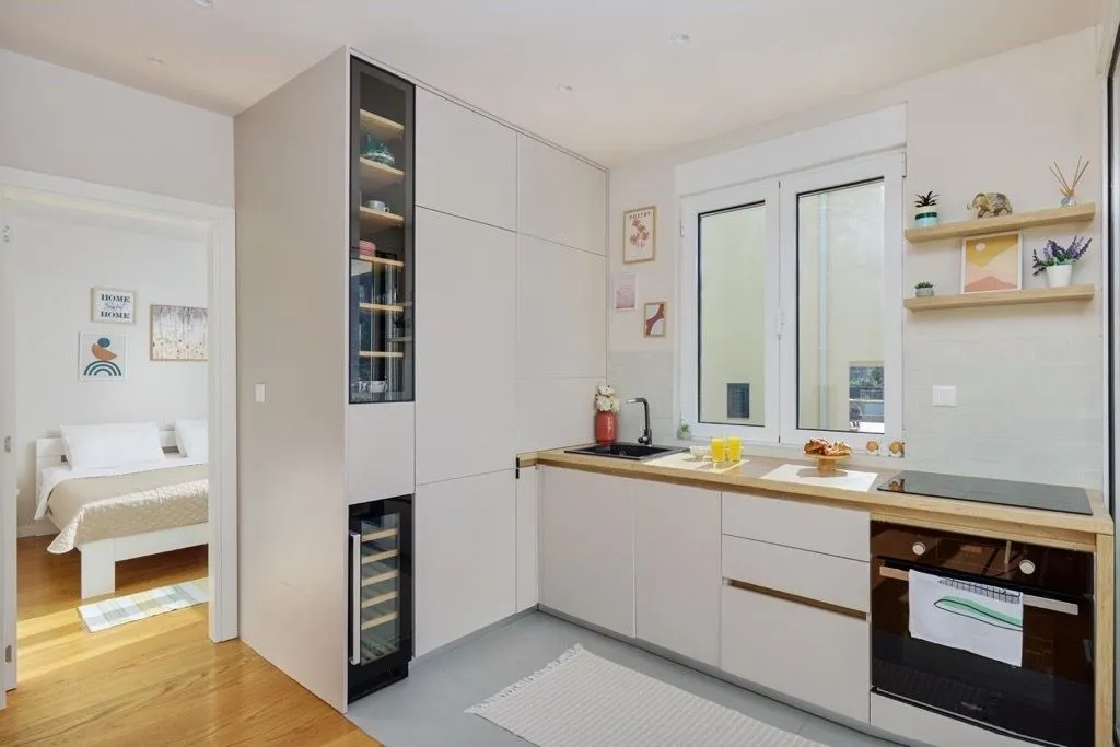 Modern kitchen in light tones with built-in appliances and a view of the bedroom.