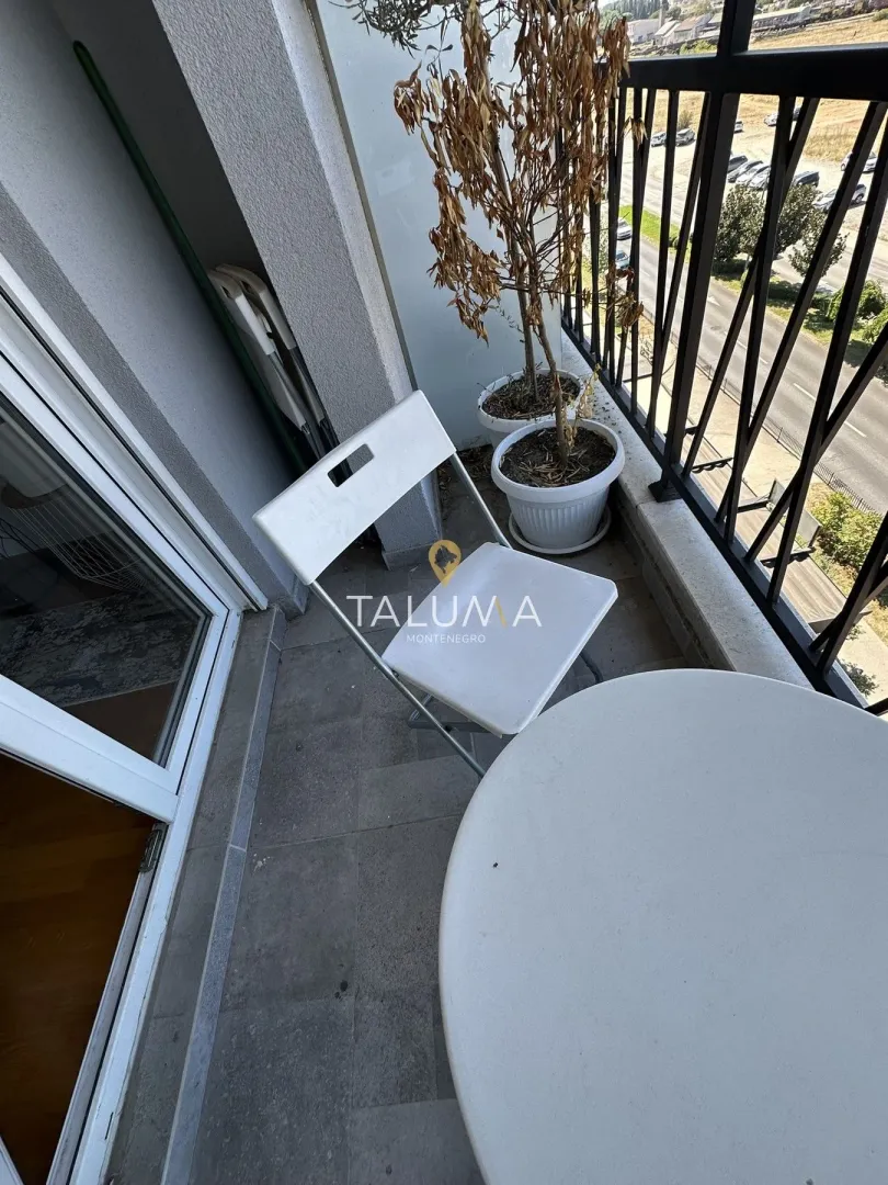 Manji namješten balkon sa stolom, stolicom i saksijama sa cvećem.