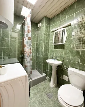 Kupatilo obloženo zelenim pločicama sa tuš kabinom, umivaonikom i toaletom. - image 5