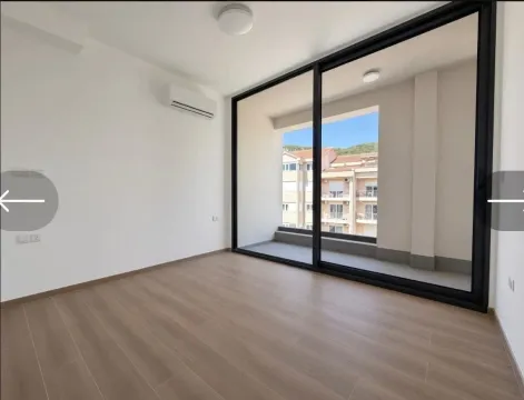 Prazna soba sa velikim staklenim balkonskim vratima i pogledom na okolne zgrade. - image 3