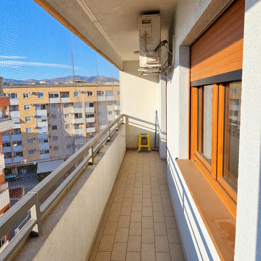Natkriveni balkon sa popločanim podom i pogledom na okolne zgrade.