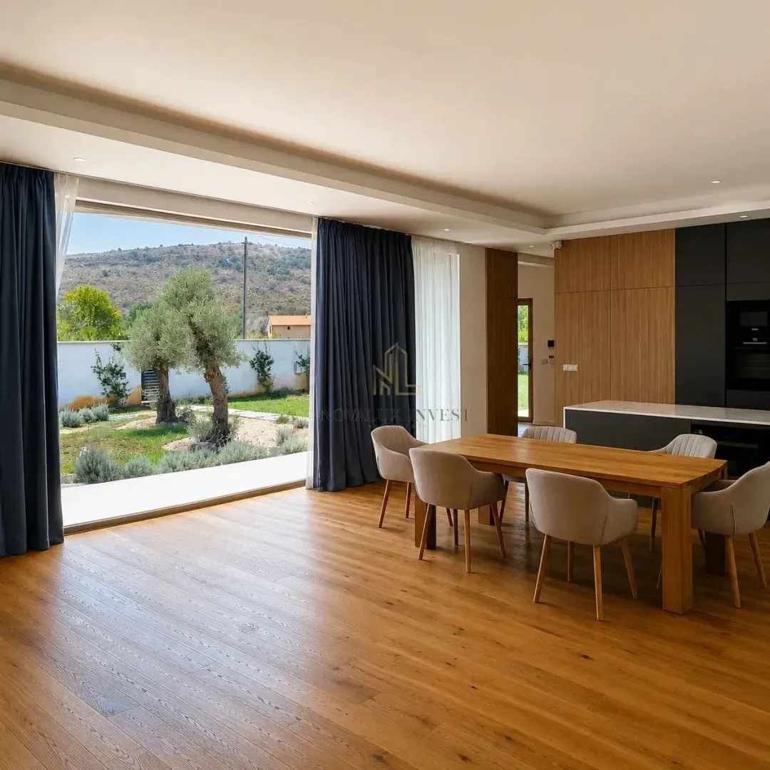Spacious living room with dining area, wooden flooring and large window overlooking the yard.
