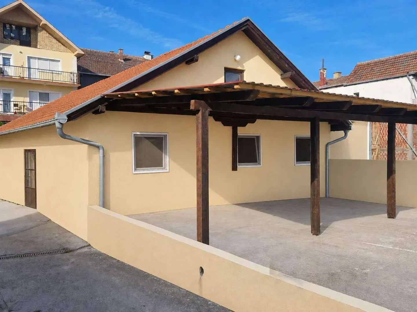 Eksterijer prizemne kuće sa nadstrešnicom i popločanim dvorištem.