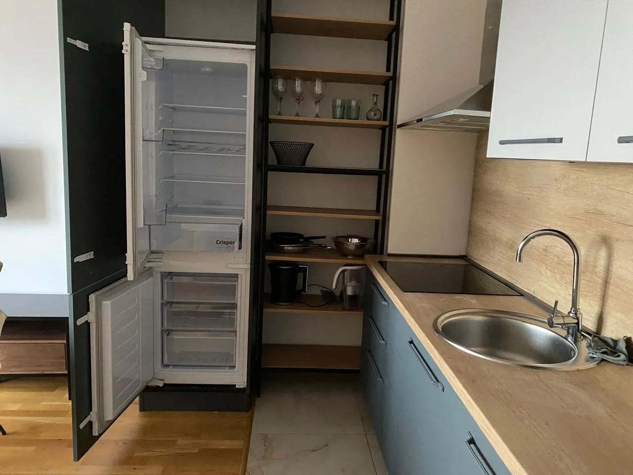 Moderna kuhinja sa otvorenim frižiderom, sudoperom i ugradnim elementima.