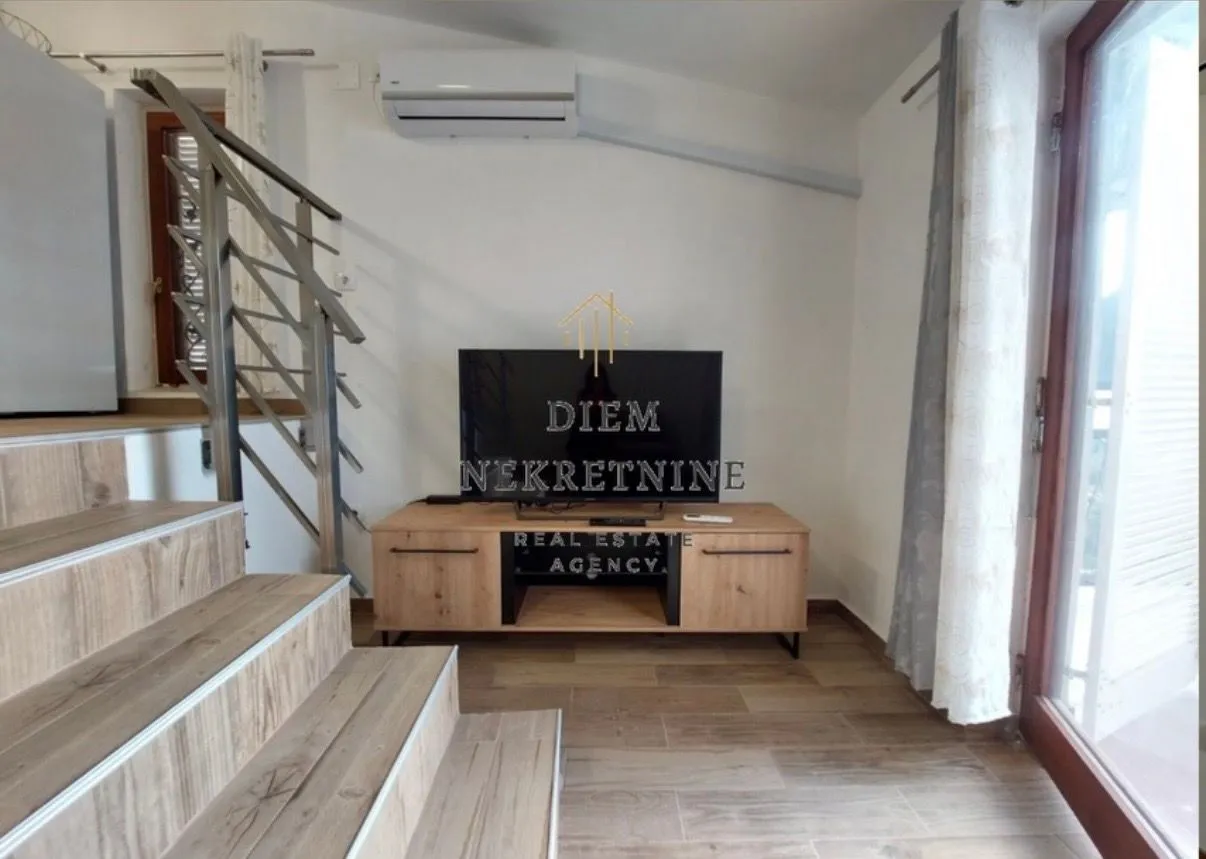 Dnevni boravak sa stepeništem i TV komodom.