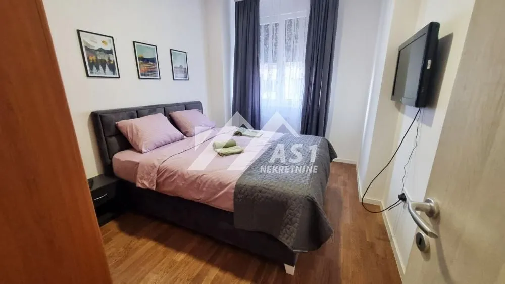 Nameštena spavaća soba sa bračnim krevetom, televizorom i prozorom.
