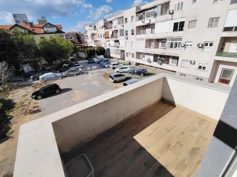 Prazan balkon sa drvenom podnom oblogom i pogledom na parking i zgrade. - image 7