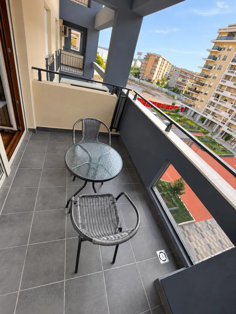 Furnished balcony with a table and two chairs overlooking surrounding buildings.
