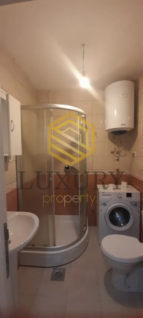 Smaller bathroom with a shower cabin, sink, toilet, and washing machine.