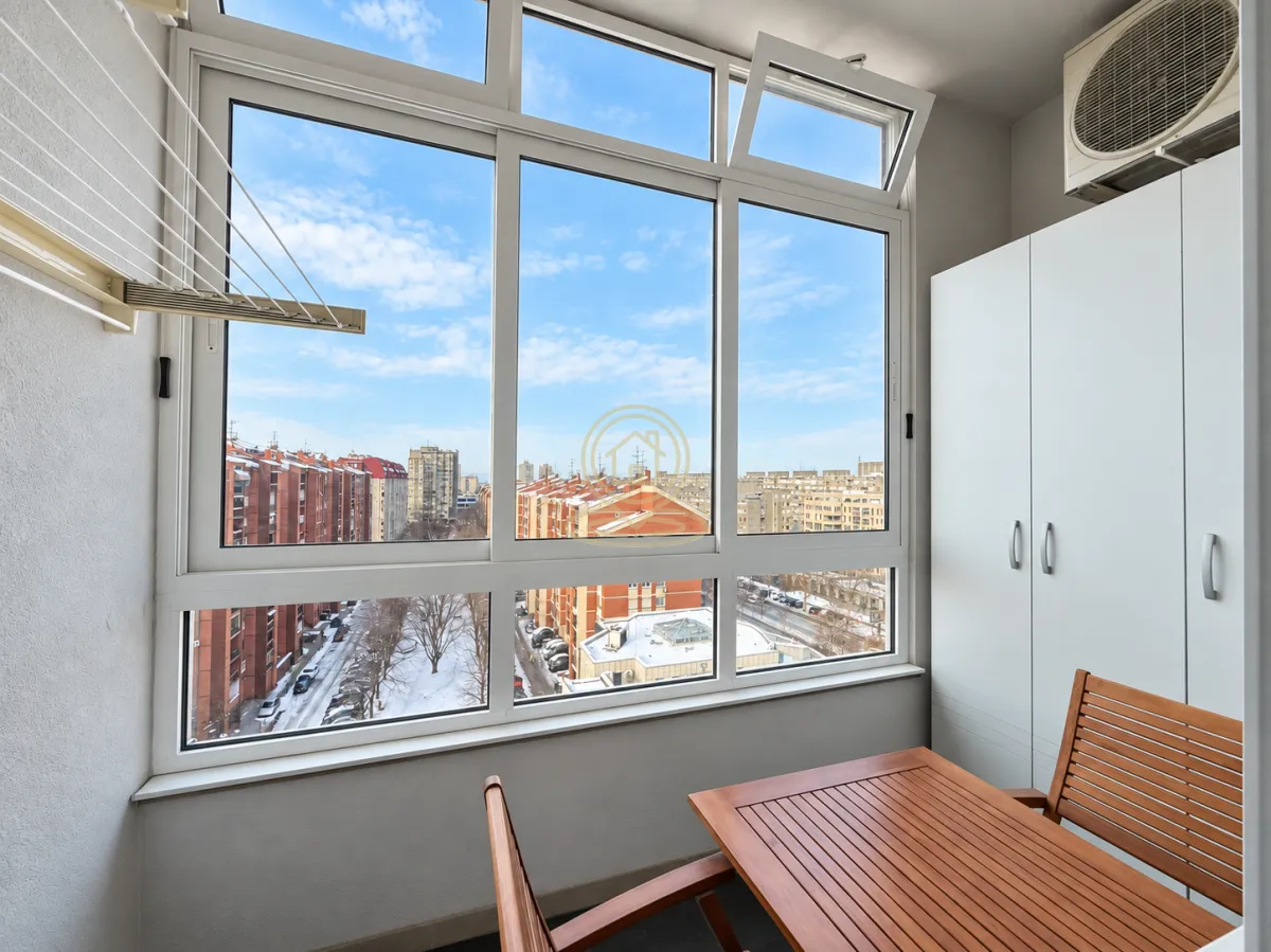 Zastakljeni balkon sa drvenim stolom i pogledom na grad.