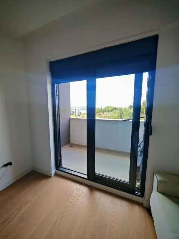 Pogled iz sobe kroz balkonska vrata prema spoljašnjem prostoru i okolini.