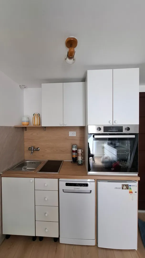 Compact kitchen with white cabinets, sink, built-in oven, and refrigerator.