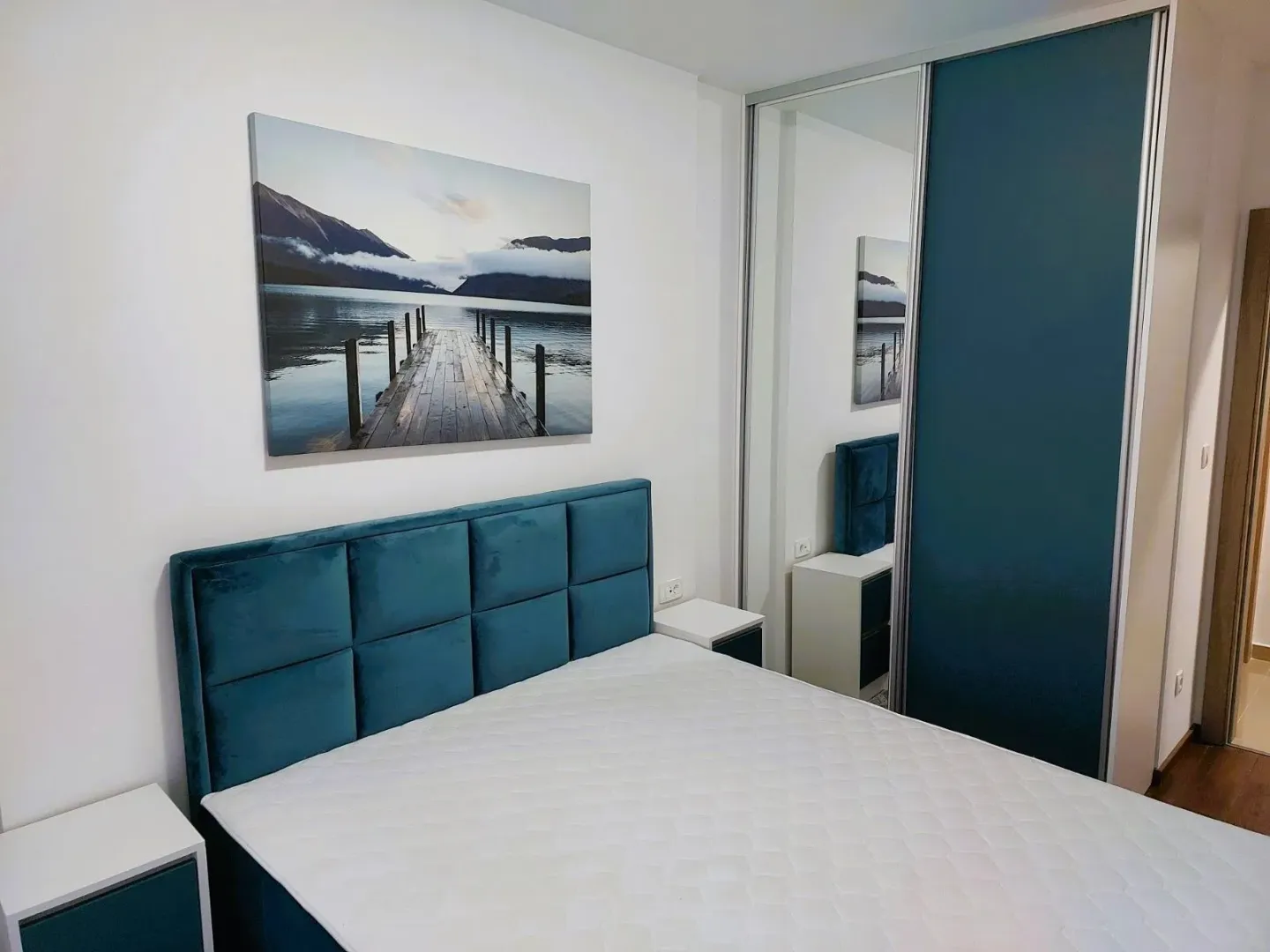 Bedroom with a blue double bed, bedside tables, and a large built-in wardrobe with a mirror.