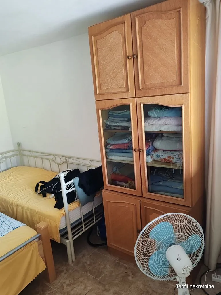 Spavaća soba sa krevetima, drvenim garderoberom i ventilatorom.