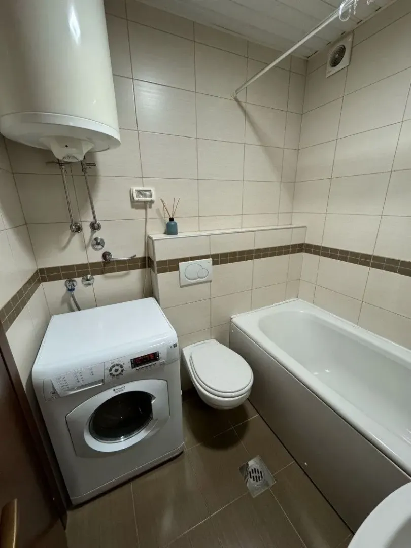 Smaller bathroom with a bathtub, toilet, and washing machine.