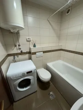 Smaller bathroom with a bathtub, toilet, and washing machine. - image 11