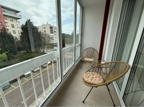 Zastakljeni balkon sa pletenim stolicama i pogledom na grad. - image 9