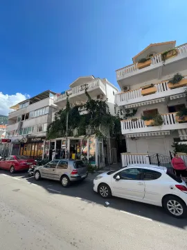 Exterior view of an apartment building with commercial space on the ground floor and parked cars in front. - image 7