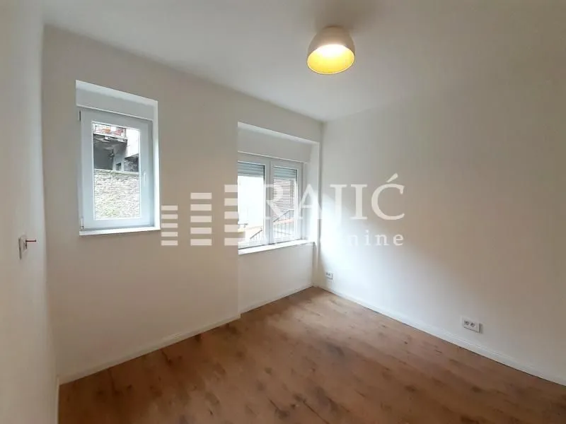 Empty room with white walls, wooden flooring and windows.