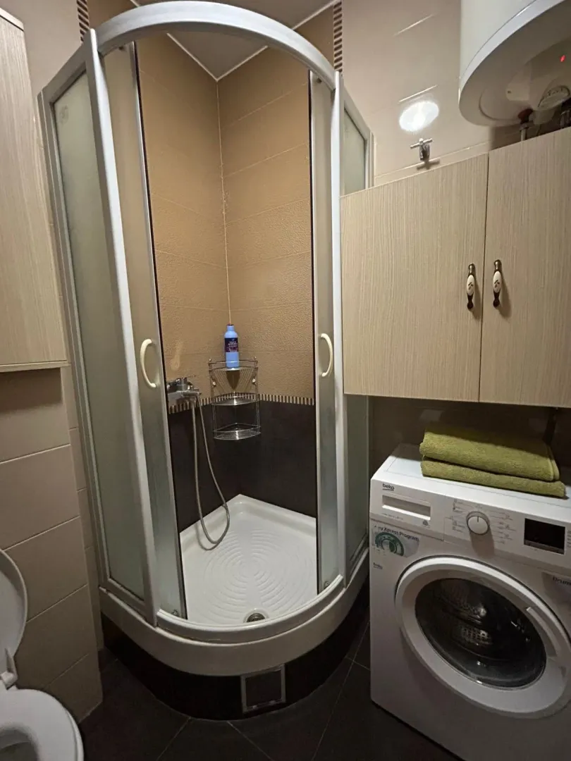Bathroom with a shower cabin, washing machine, and wall cabinet.