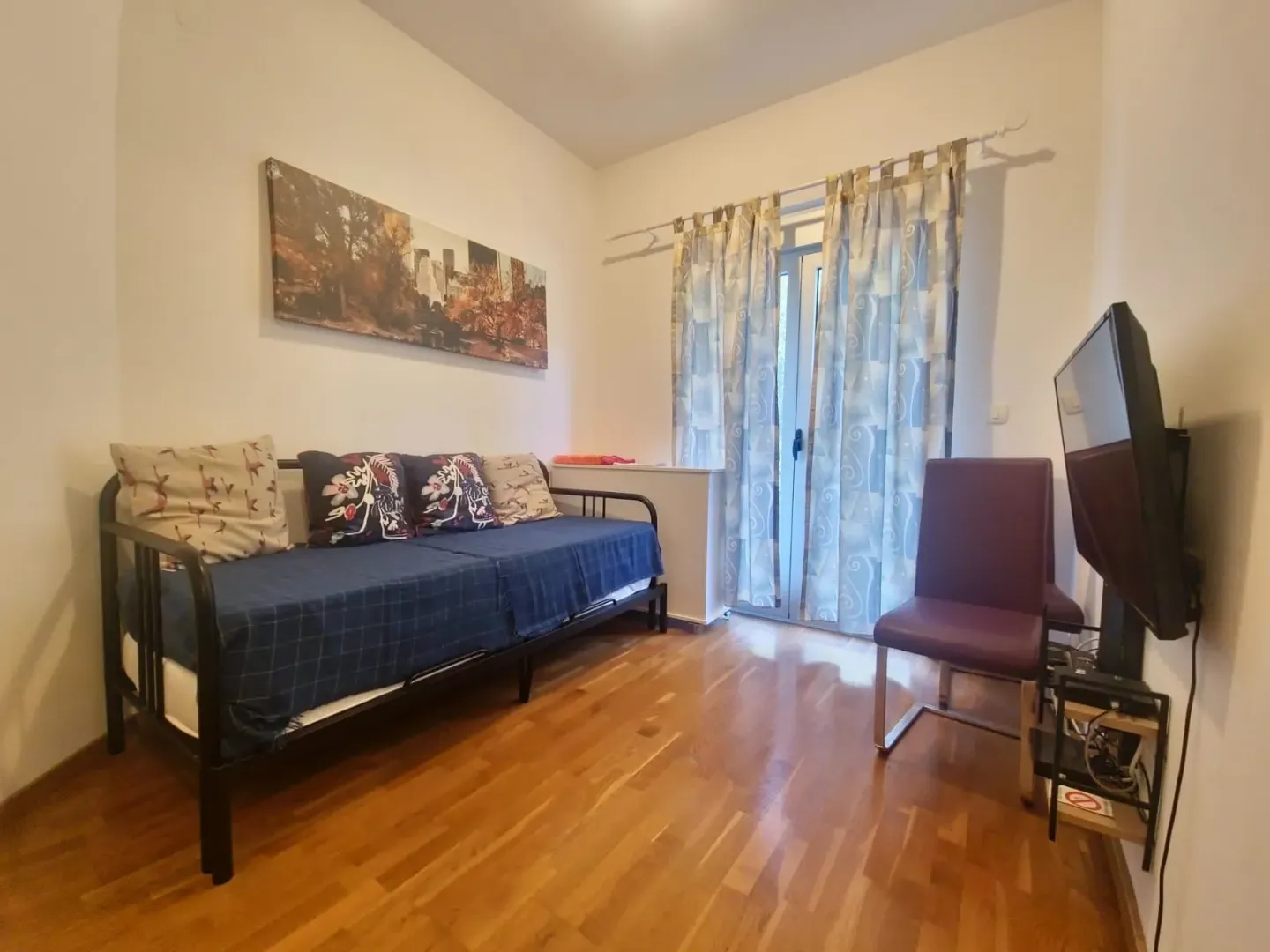 Living room with a sofa bed, television, and balcony access.