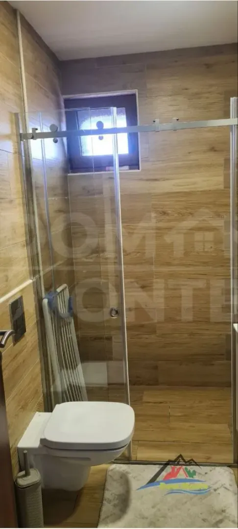 Kupatilo sa tuš kabinom obloženo keramičkim pločicama u imitaciji drveta.