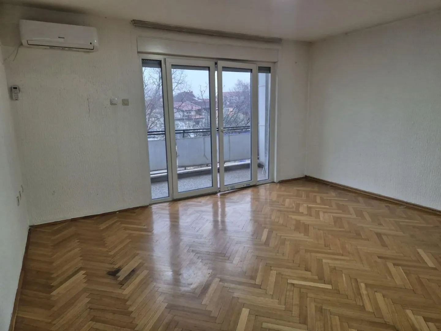 Empty room with parquet flooring and balcony access.
