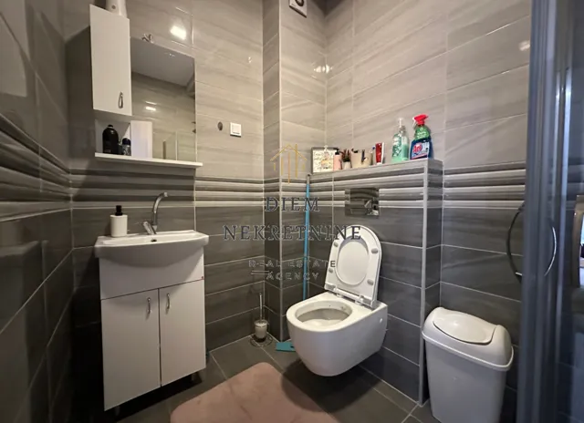 Moderne kupatilo obloženo sivim pločicama sa umivaonikom i wc šoljom.