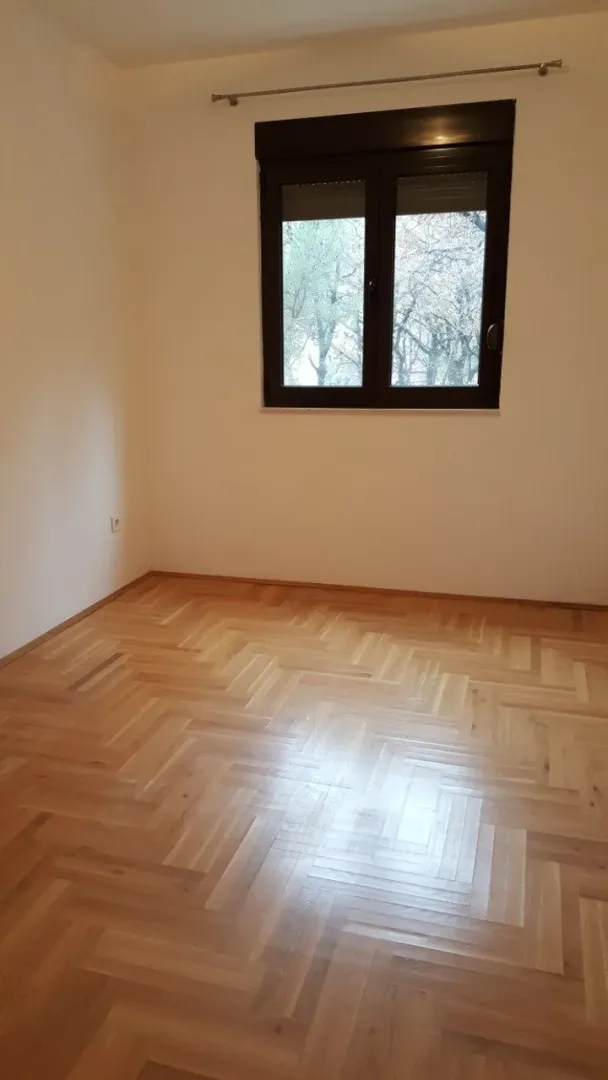 An empty room with parquet flooring and a window.