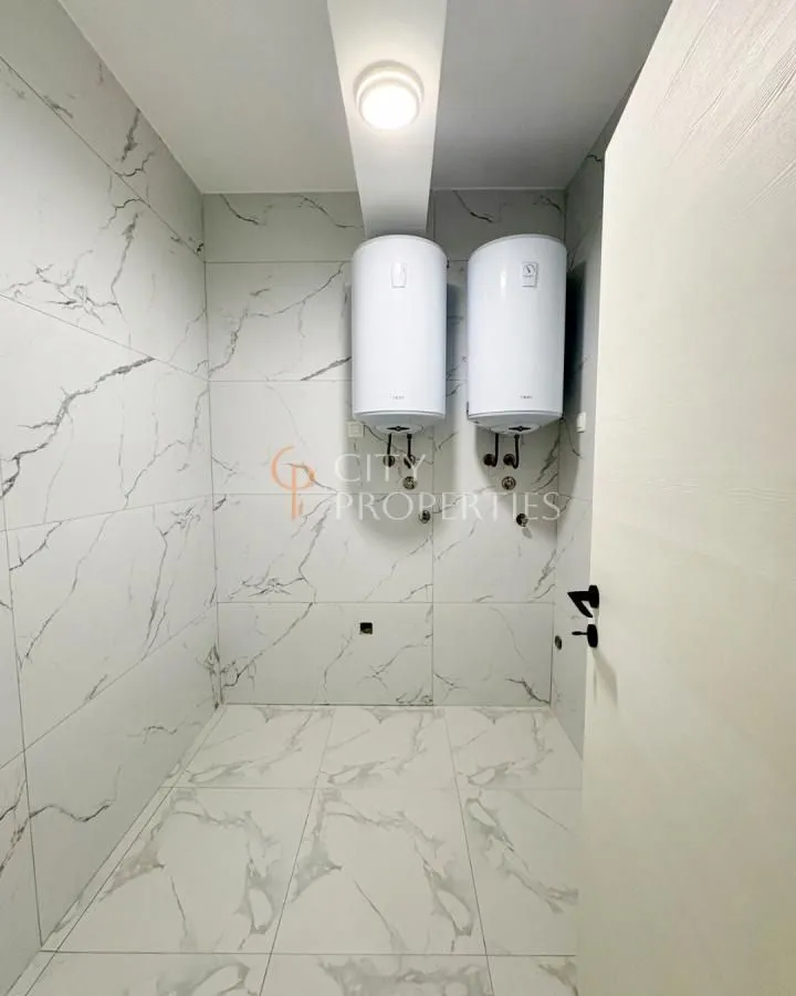 Bathroom tiled with marble-pattern tiles featuring two electric water heaters on the wall.