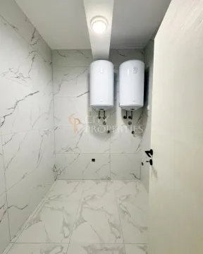 Bathroom tiled with marble-pattern tiles featuring two electric water heaters on the wall. - image 8